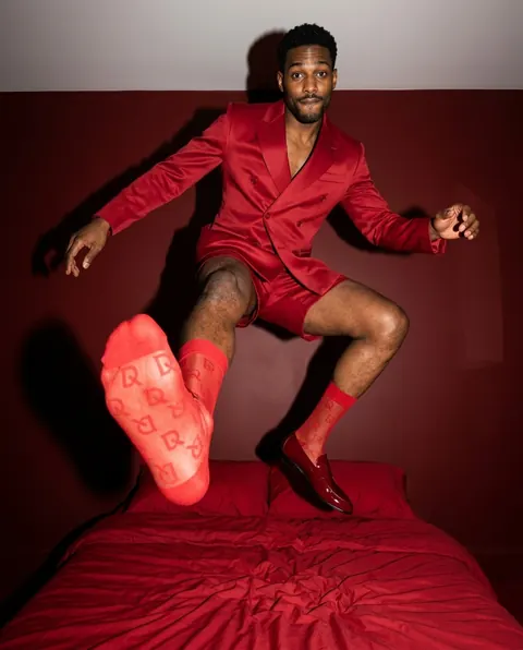 Omar im roten Anzug springt in D-SoQs-Socken auf ein Bett